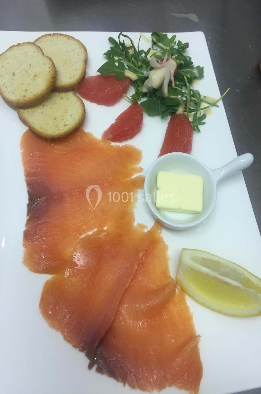 Assiette de saumon fumé avec tranches de pain, salade verte, quartiers de pamplemousse, beurre et citron.