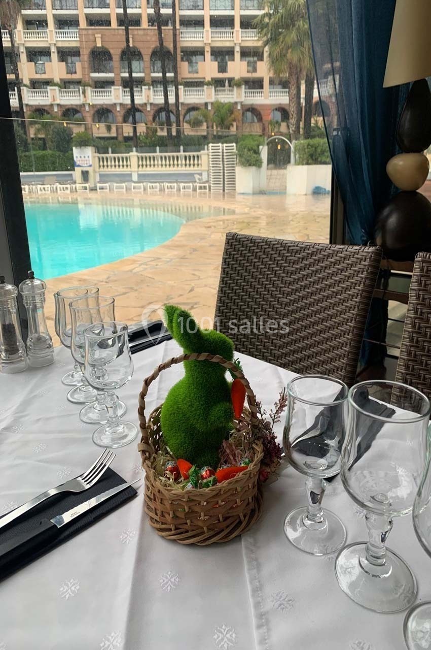 Panier décoratif avec un lapin vert en mousse et des bonbons sur une table dressée près d'une piscine extérieure.