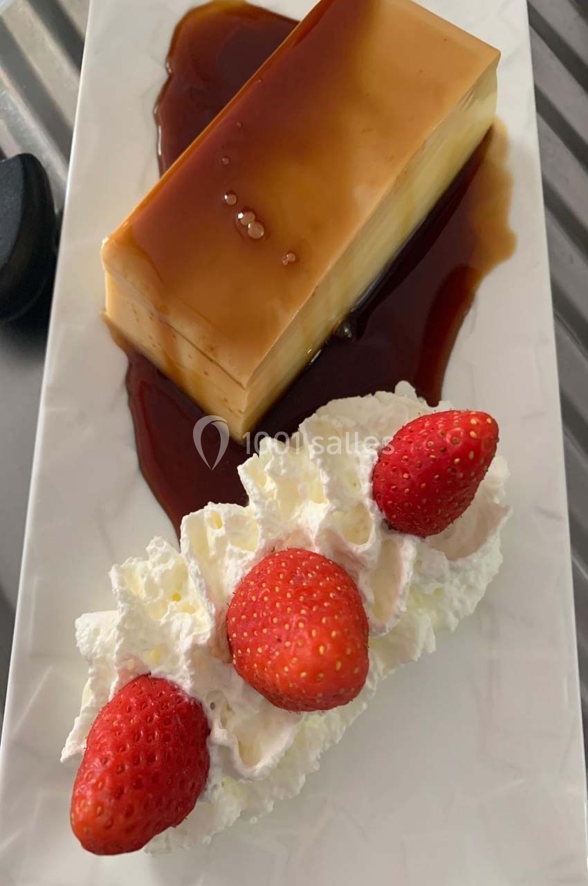 Flan nappé de caramel accompagné de chantilly décorée de fraises fraîches sur une assiette blanche.