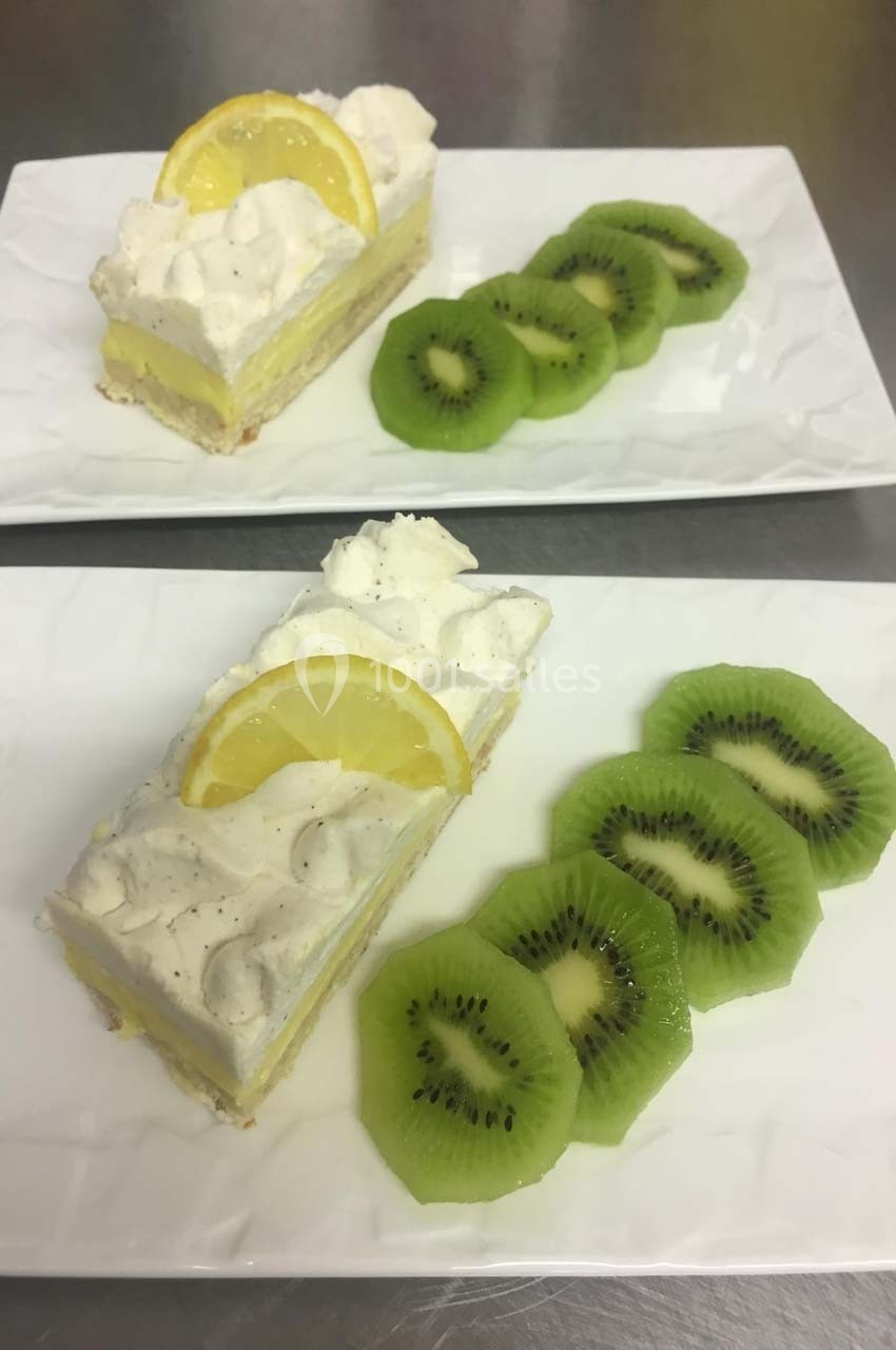 Deux assiettes contenant une part de dessert citronné avec une tranche de citron et des rondelles de kiwi en accompagnement.