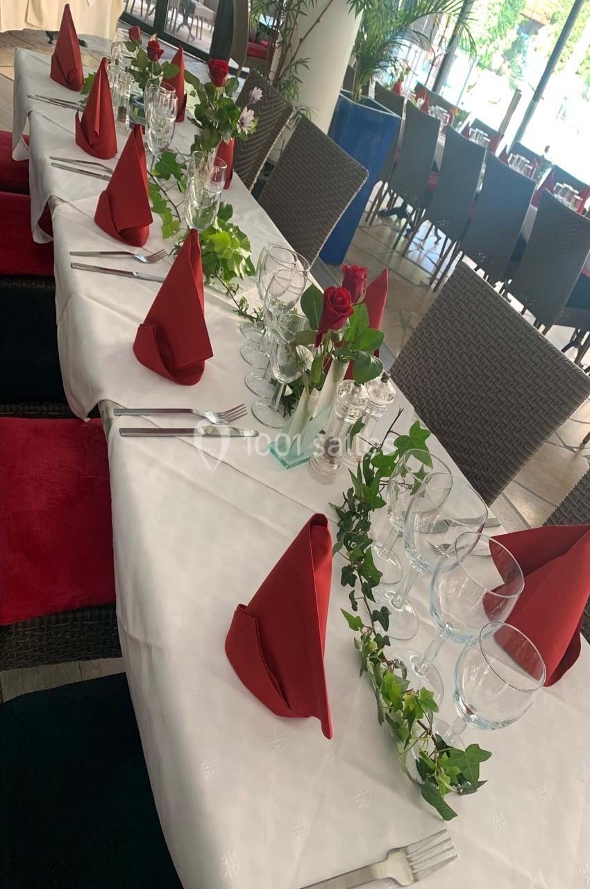 Table dressée avec nappes blanches, serviettes rouges pliées, verres, couverts, roses et guirlandes de lierre.