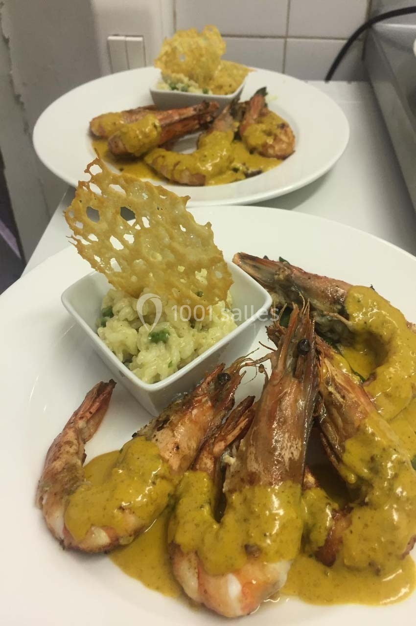 Assiette de crevettes nappées de sauce jaune, accompagnées de risotto et d'une tuile croustillante.