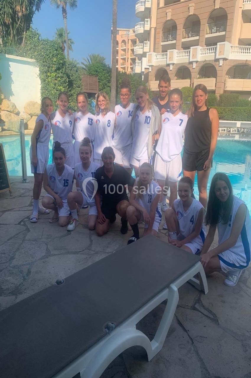 Un groupe de jeunes joueuses de basketball en tenue blanche pose avec des adultes près d'une piscine en extérieur.
