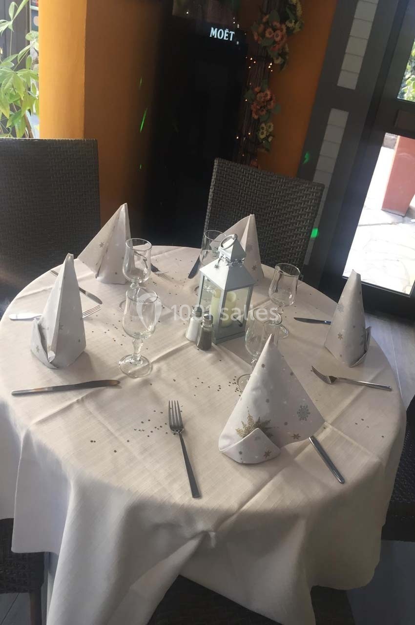 Table dressée avec une nappe blanche, serviettes pliées, verres, couverts, une lanterne centrale et décorations discrètes.