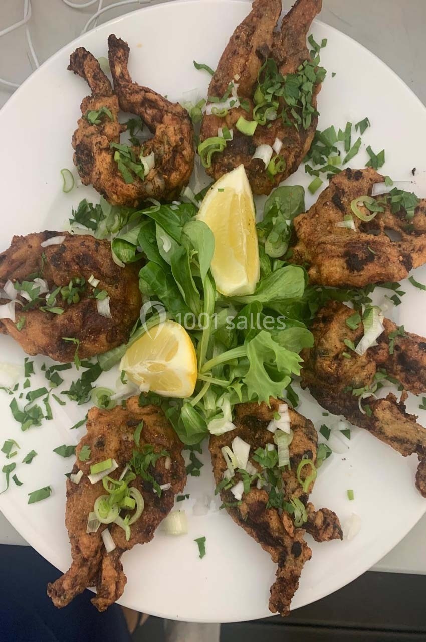 Assiette de cuisses de grenouilles grillées garnies de citron, salade verte et herbes fraîches.