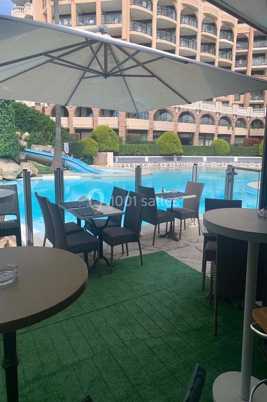 Terrasse avec tables et chaises sous des parasols, donnant sur une piscine entourée d'un bâtiment résidentiel.