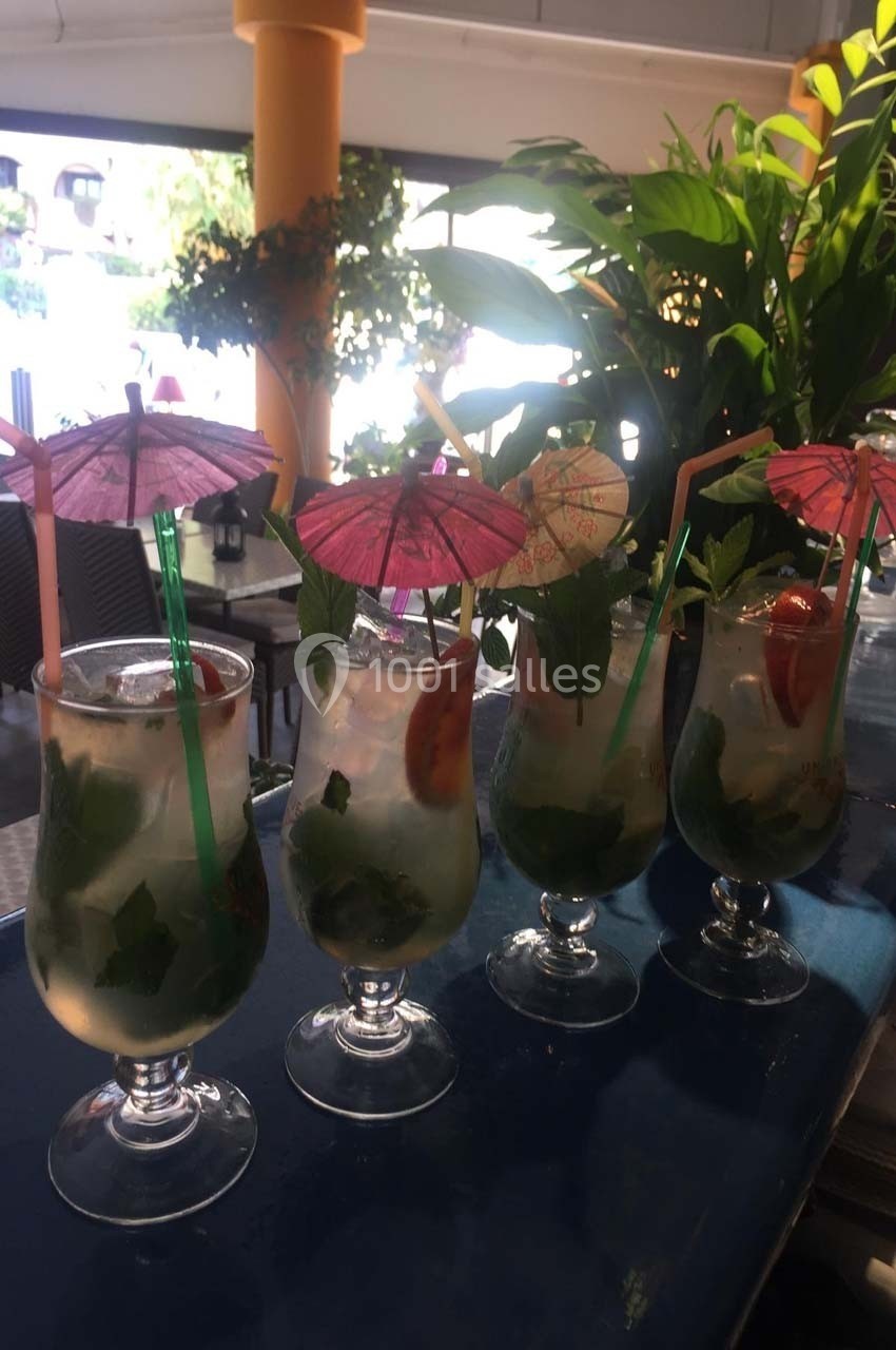 Quatre verres de mojitos garnis de feuilles de menthe, rondelles de citron et ombrelles colorées sur un bar.