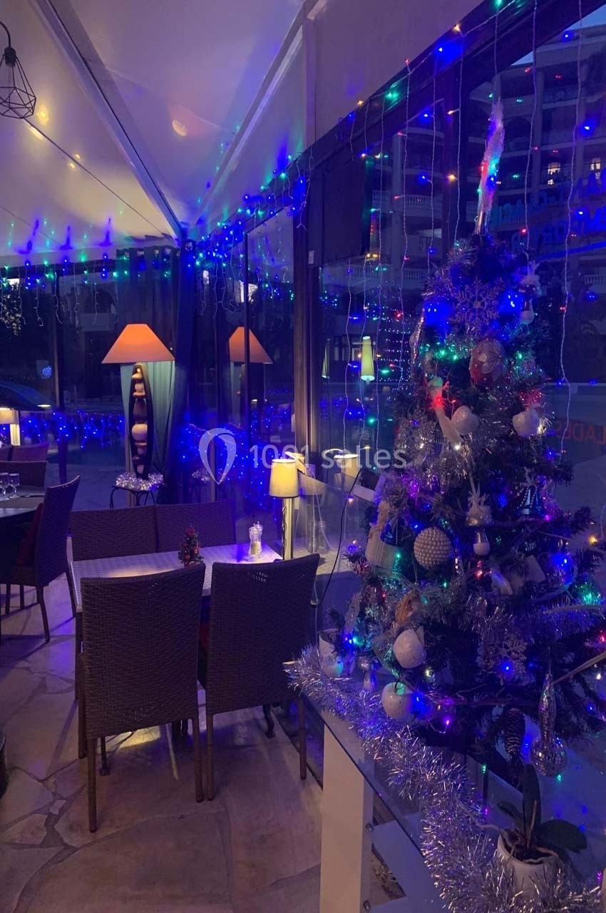 Terrasse couverte décorée pour Noël avec guirlandes lumineuses, sapin décoré et tables dressées pour le dîner.