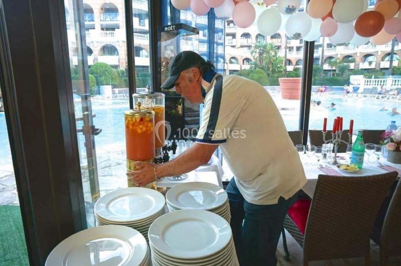 Un homme remplit un distributeur de boisson près d'une table dressée, avec une piscine en arrière-plan.