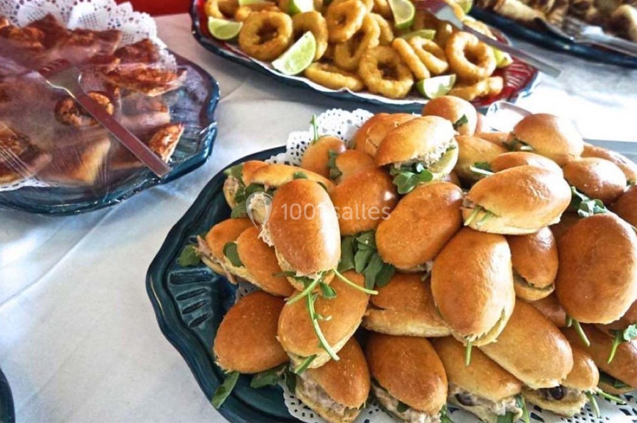 Plateau de mini-sandwichs garnis de roquette, entouré de beignets de calamars et autres amuse-bouches sur une table.