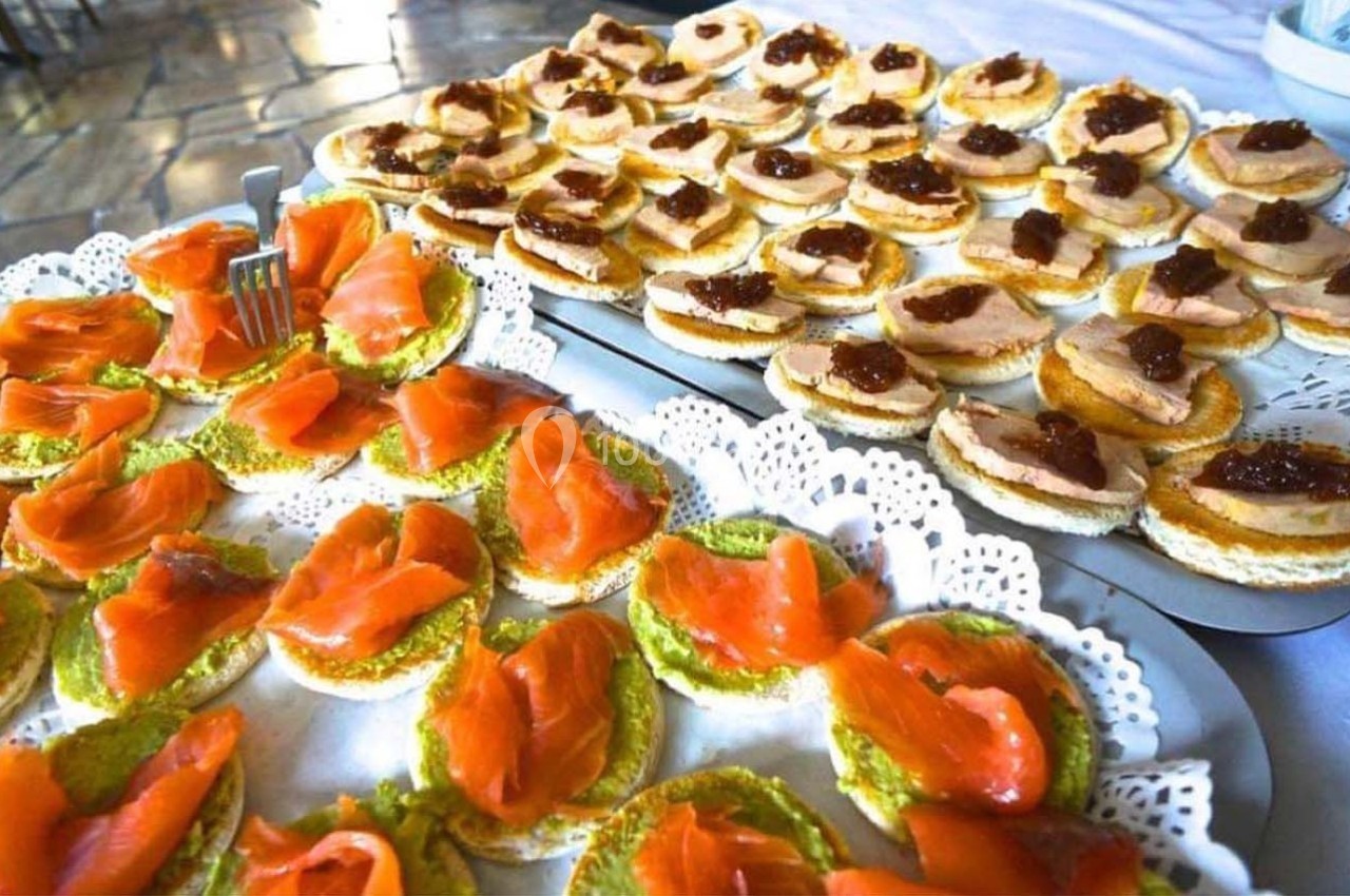 Plateaux de canapés garnis de saumon fumé et de foie gras avec confiture, présentés sur des nappes blanches.