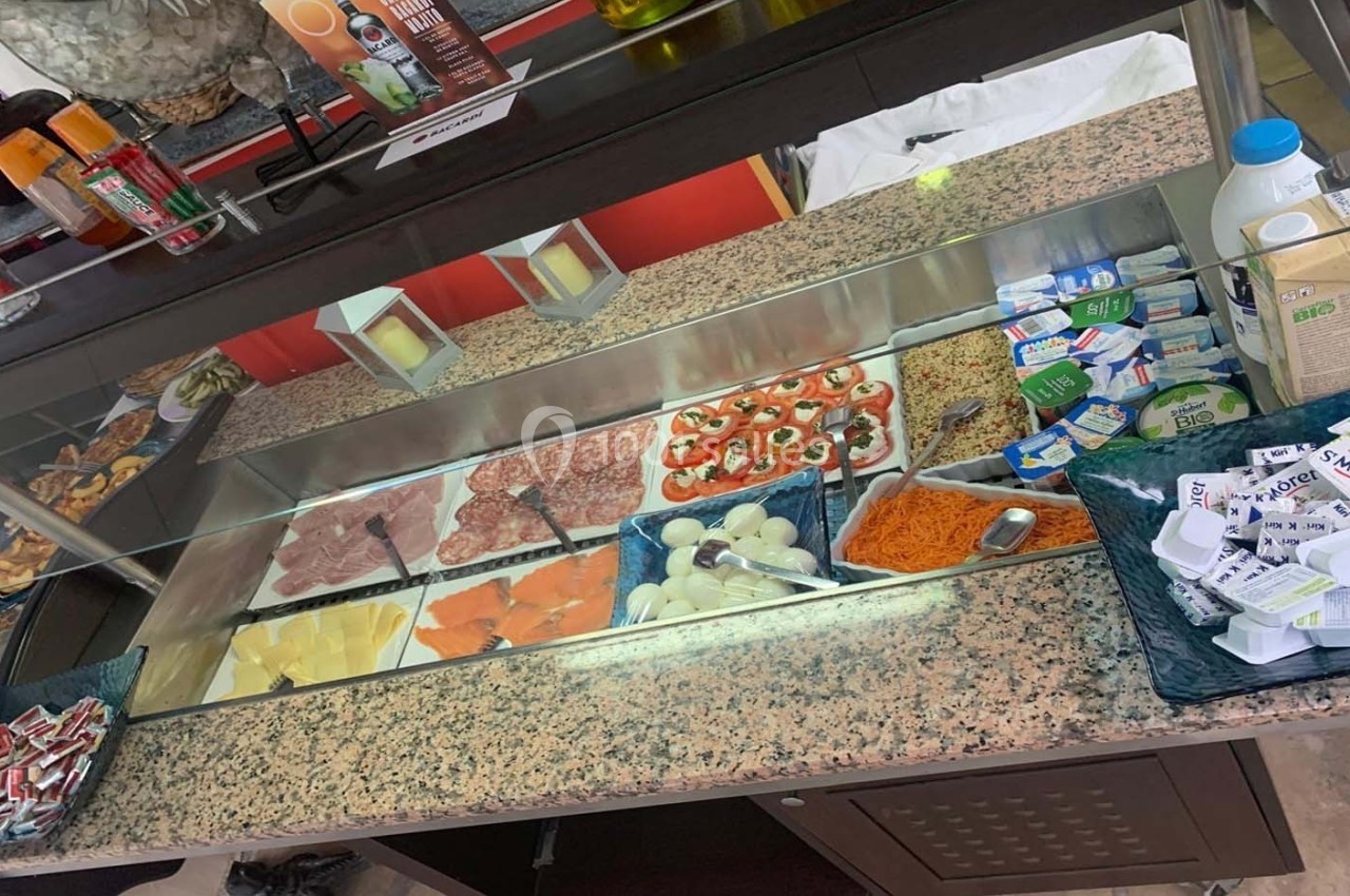 Vitrine réfrigérée présentant un assortiment de charcuteries, fromages, légumes et condiments variés.