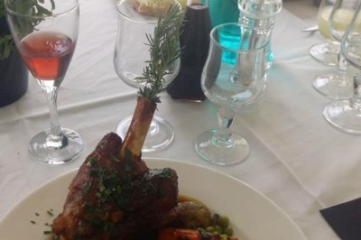 Assiette garnie d'un jarret d'agneau, légumes, pommes de terre rôties, sur une table dressée avec boissons et décorations.