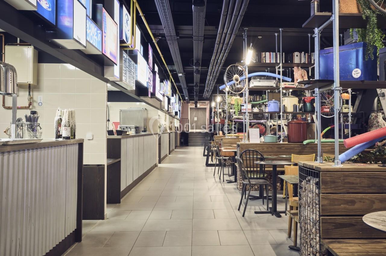 Intérieur d'un espace de restauration moderne avec tables, chaises et comptoirs alignés sous un éclairage lumineux.