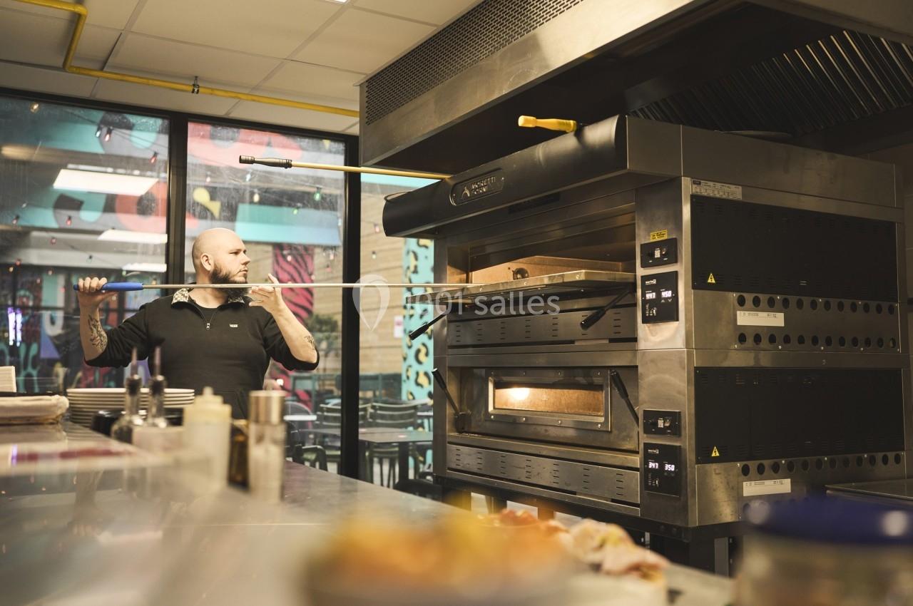 Un cuisinier utilise une pelle pour enfourner ou retirer une pizza dans un four professionnel dans une cuisine ouverte.