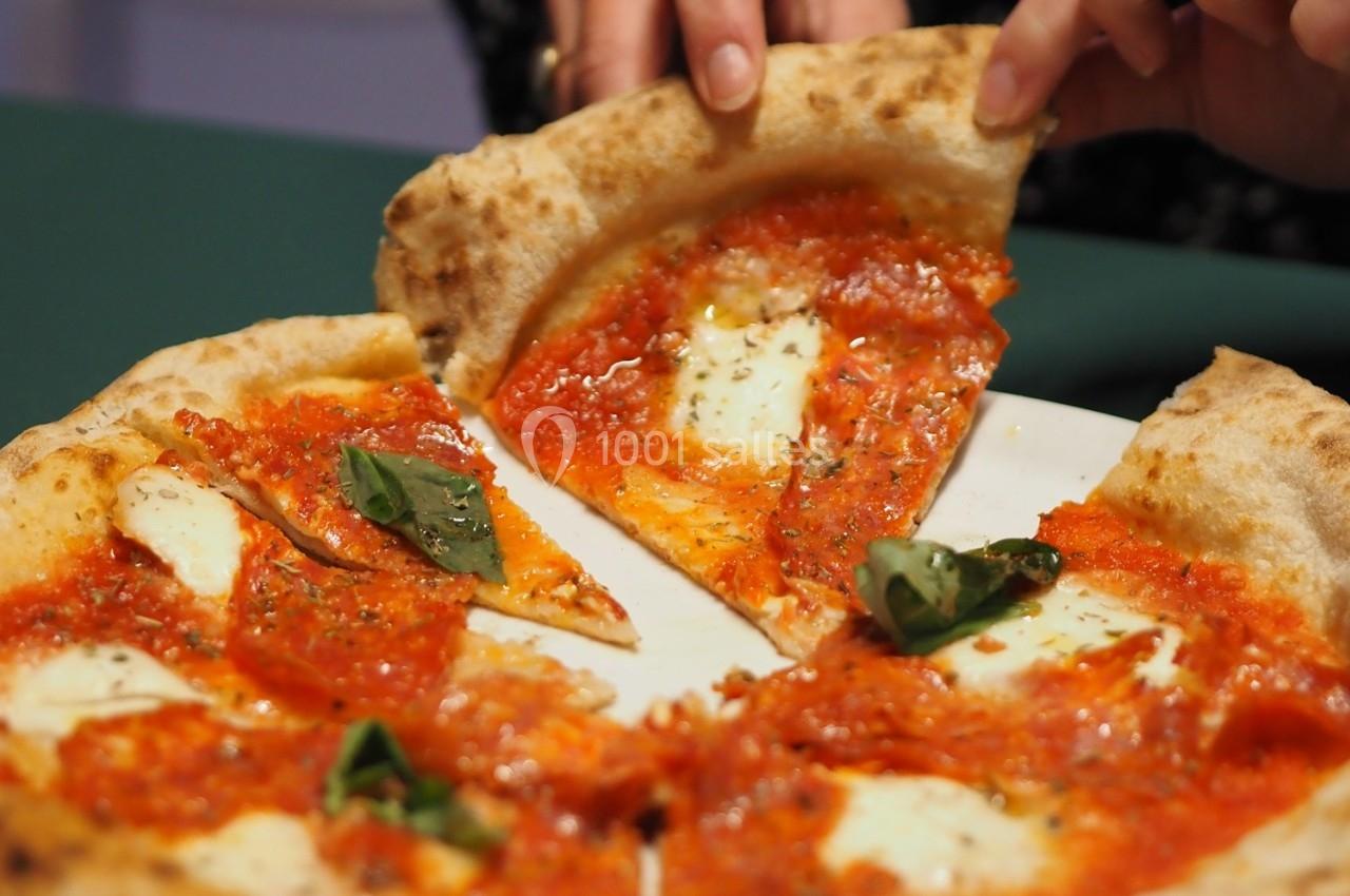 Part de pizza margherita avec sauce tomate, mozzarella fondue et feuilles de basilic, tenue par une main.