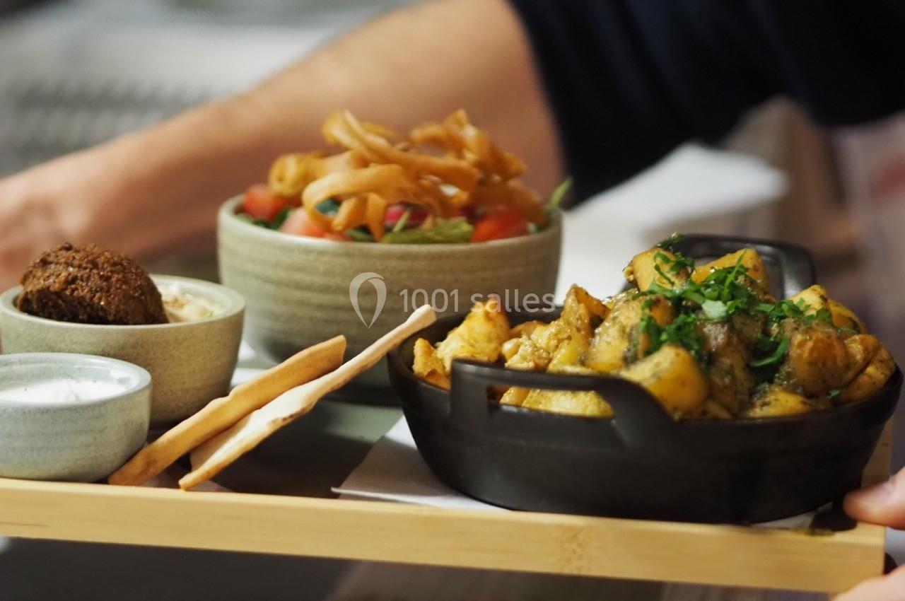 Plateau de mets variés comprenant pommes de terre rôties, falafels, sauces et salade colorée dans des bols.