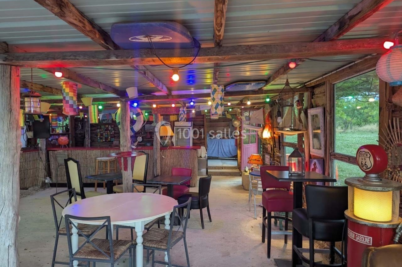 Intérieur d'un bar rustique avec tables, chaises, décorations colorées et éclairage chaleureux.