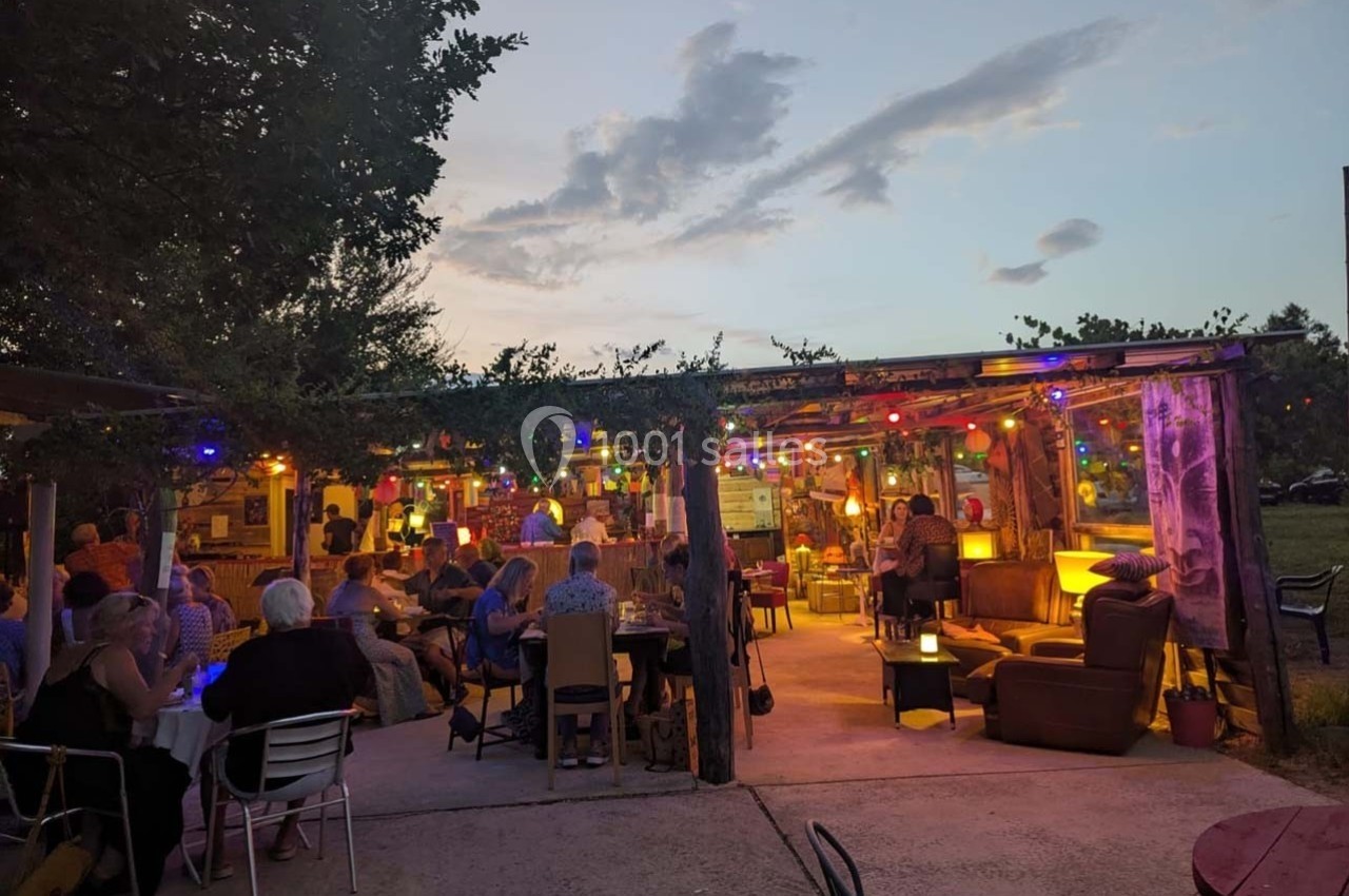 Terrasse extérieure éclairée par des guirlandes lumineuses, avec des personnes assises et discutant en soirée.