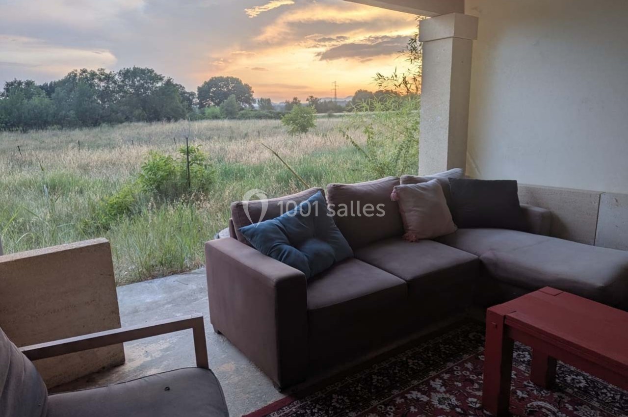 Canapé d'angle avec coussins sur une terrasse couverte, vue sur un champ au coucher du soleil.