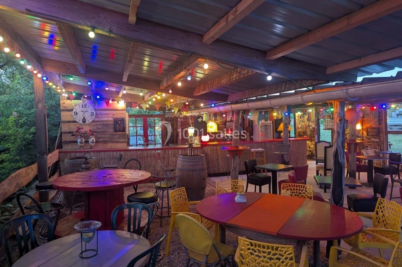 Terrasse couverte décorée de guirlandes lumineuses colorées, avec tables et chaises de styles variés.