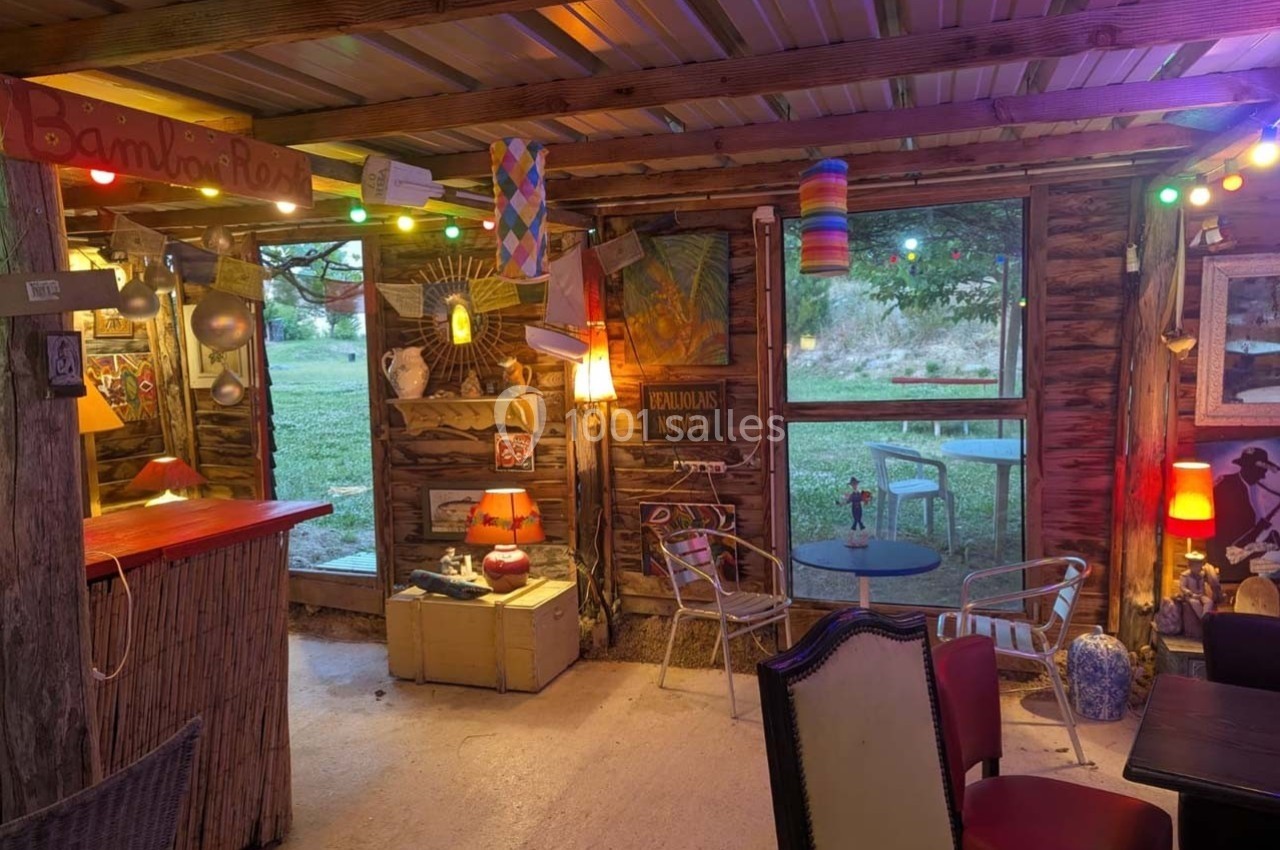 Intérieur d'un café rustique avec décoration éclectique, éclairage coloré et vue sur un espace extérieur verdoyant.