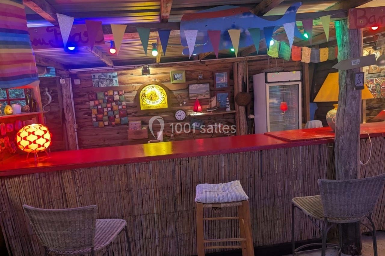 Comptoir de bar en bois décoré de guirlandes lumineuses colorées, avec tabourets et ambiance chaleureuse.