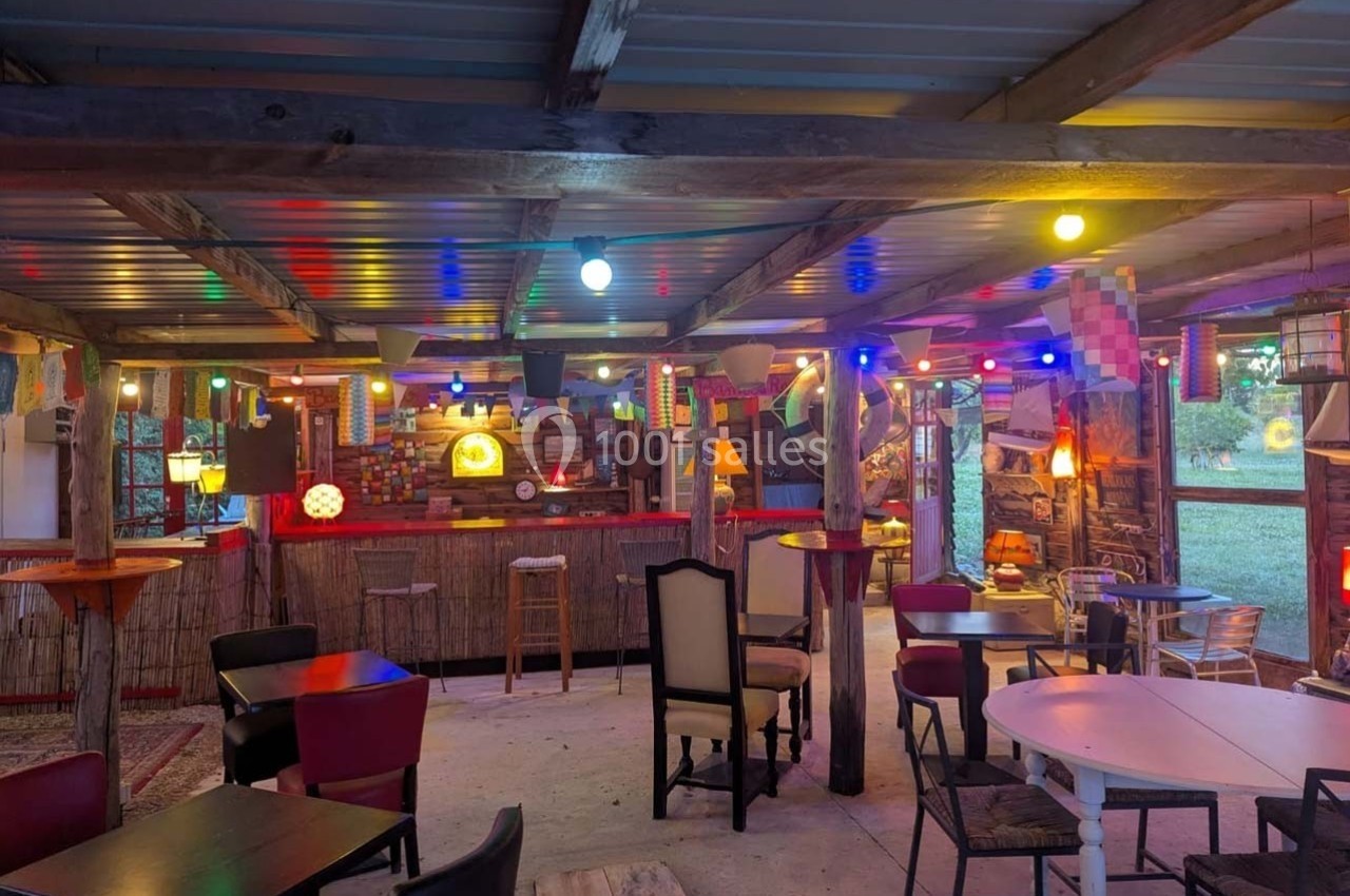 Espace intérieur coloré avec tables, chaises et éclairage multicolore, ambiance conviviale et rustique.