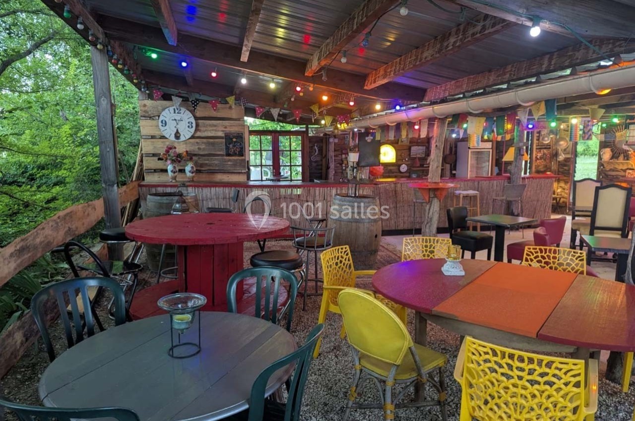 Terrasse couverte décorée avec des tables colorées, des chaises variées et des guirlandes lumineuses suspendues.