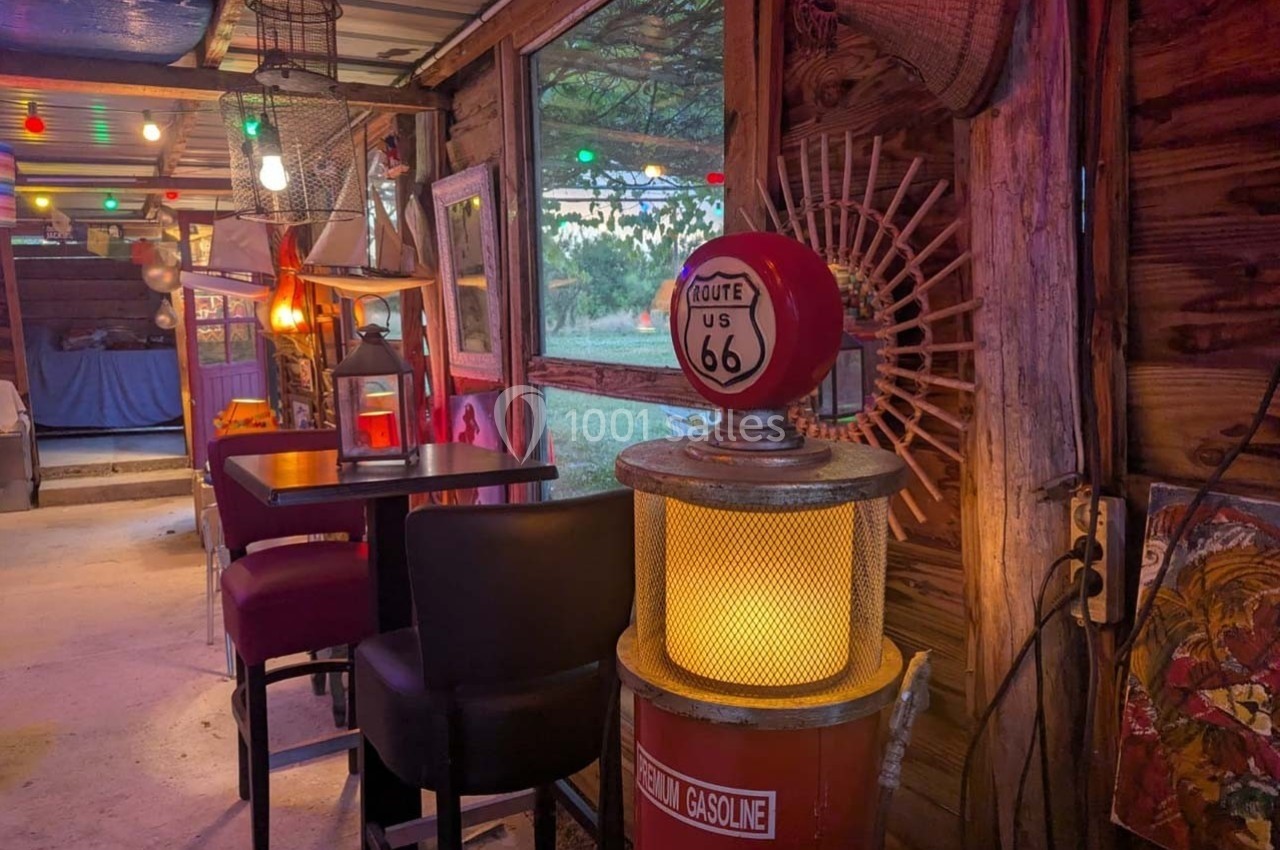 Intérieur rustique avec mobilier simple, éclairage coloré et pompe vintage Route 66 près d'une fenêtre.