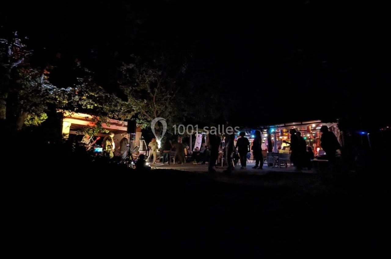 Groupe de personnes rassemblées en soirée près de bâtiments éclairés, entourés de végétation sombre.