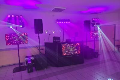 Salle de réception décorée pour un événement, avec tables rondes dressées, nappes blanches et éléments végétaux.