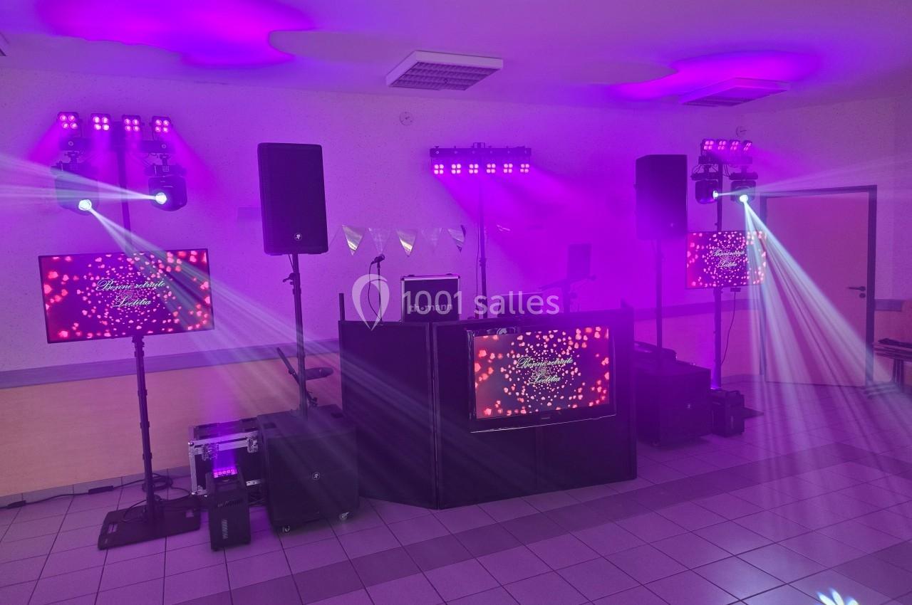 Installation de matériel de sonorisation et d'éclairage avec écrans et projecteurs dans une salle éclairée en violet.