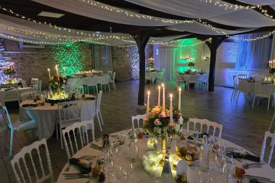 Salle de réception décorée pour un événement, avec tables rondes dressées, nappes blanches et éléments végétaux.