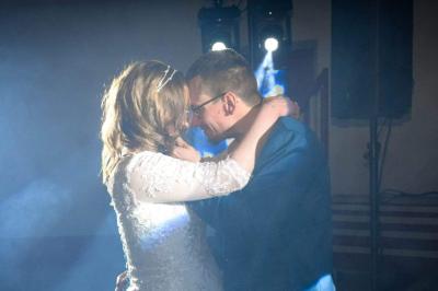 Salle de réception décorée pour un événement, avec tables rondes dressées, nappes blanches et éléments végétaux.