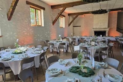 Salle de réception décorée pour un événement, avec tables rondes dressées, nappes blanches et éléments végétaux.