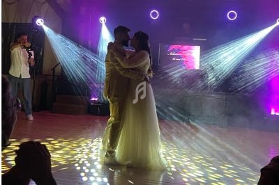 Un couple danse sous des projecteurs colorés sur une piste éclairée, avec un DJ en arrière-plan.