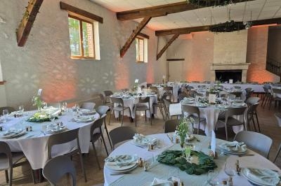 Salle de réception lumineuse avec tables rondes dressées, nappes blanches et décorations végétales.