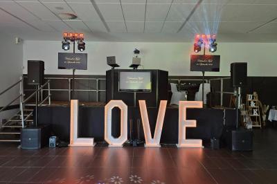 Salle de réception décorée pour un événement, avec tables rondes dressées, nappes blanches et éléments végétaux.