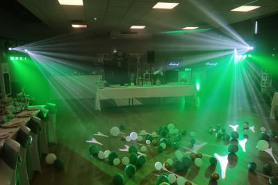 Salle de réception décorée pour un événement, avec tables rondes dressées, nappes blanches et éléments végétaux.
