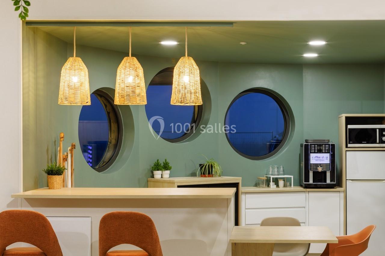 Cuisine moderne avec suspensions en rotin, fenêtres rondes, mobilier minimaliste et machine à café intégrée.