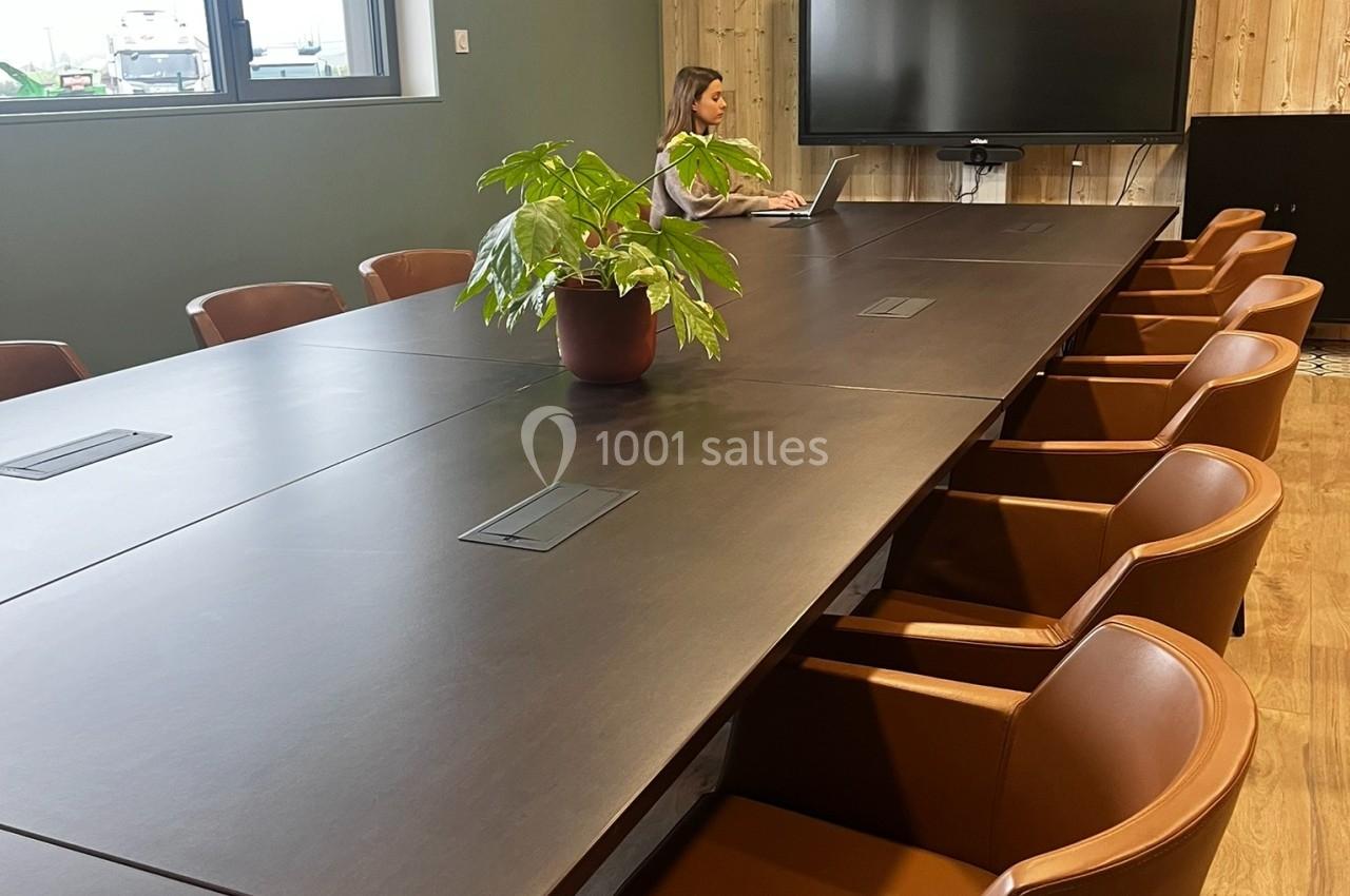 Salle de réunion avec une grande table en bois sombre, des chaises en cuir marron, une plante et un écran au mur.