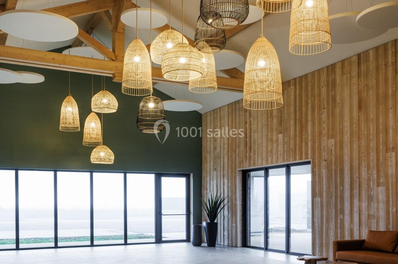 Suspensions en osier éclairées dans une grande pièce avec murs en bois, plafond haut et larges baies vitrées.