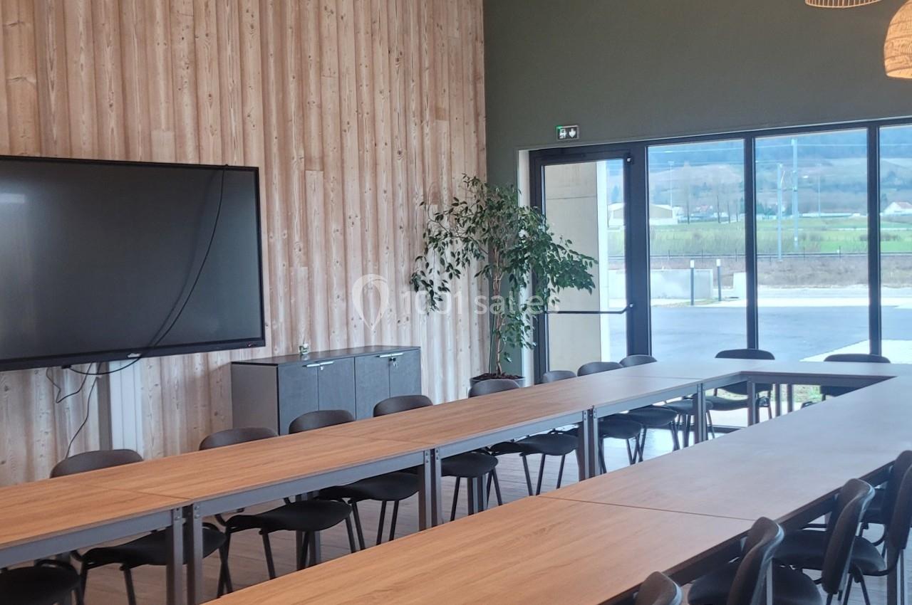 Salle de réunion lumineuse avec de longues tables en bois, chaises noires, luminaires suspendus et grande baie vitrée.