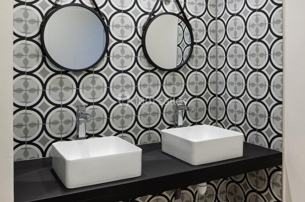 Deux lavabos blancs avec robinets modernes sur un plan noir, devant un mur carrelé à motifs géométriques.