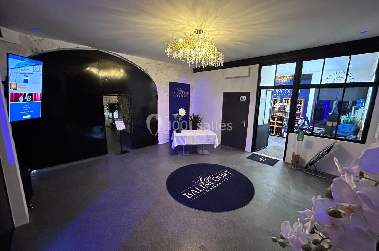 Entrée d'un espace événementiel avec un tapis rond au sol, un lustre suspendu et des portes vitrées donnant sur une salle.