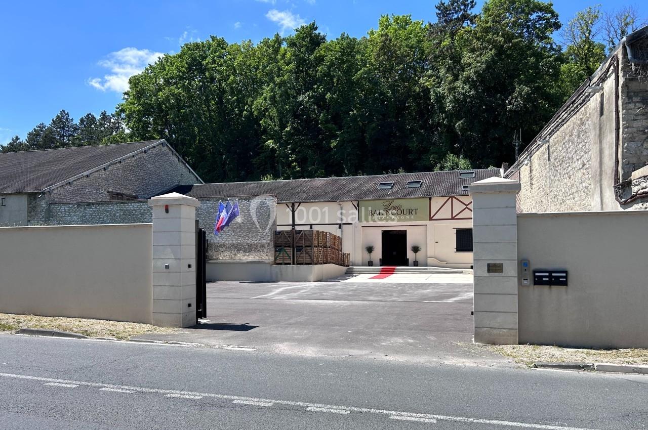 Entrée d'un bâtiment avec façade en pierre, drapeaux français et européen, entouré de murs et d'arbres en arrière-plan.