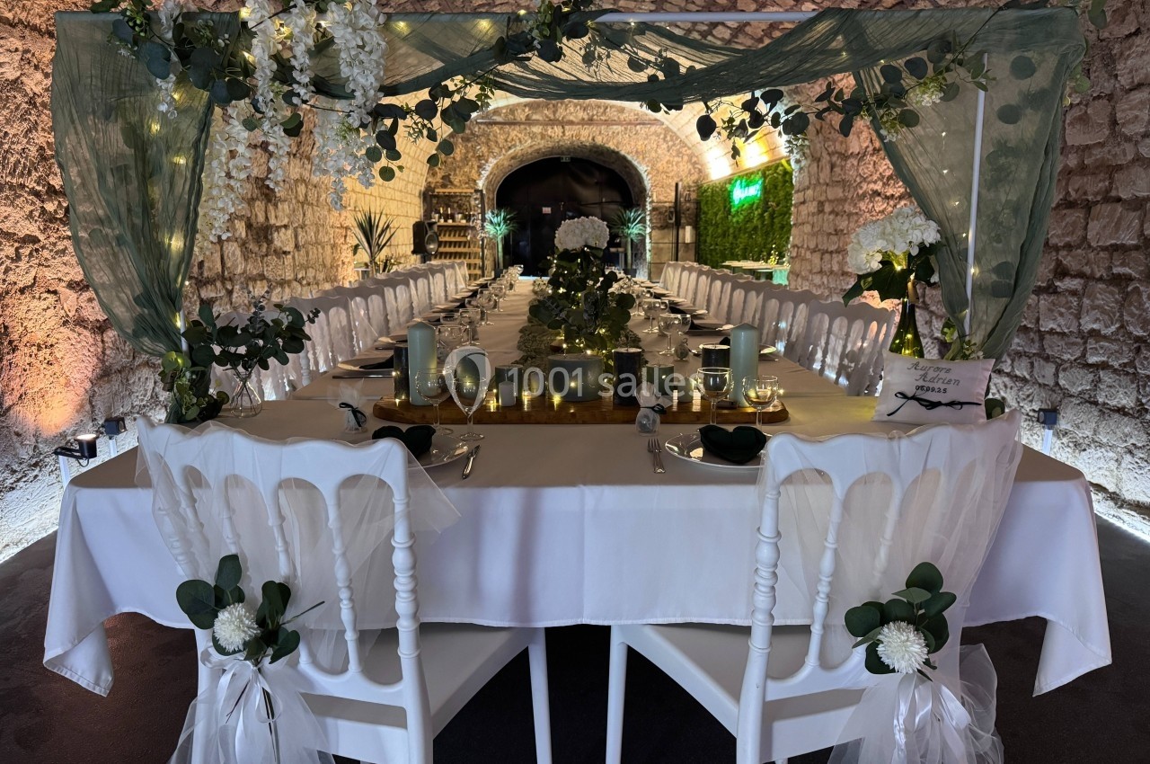 Table décorée pour un dîner élégant sous une voûte en pierre, ornée de fleurs, bougies et guirlandes lumineuses.