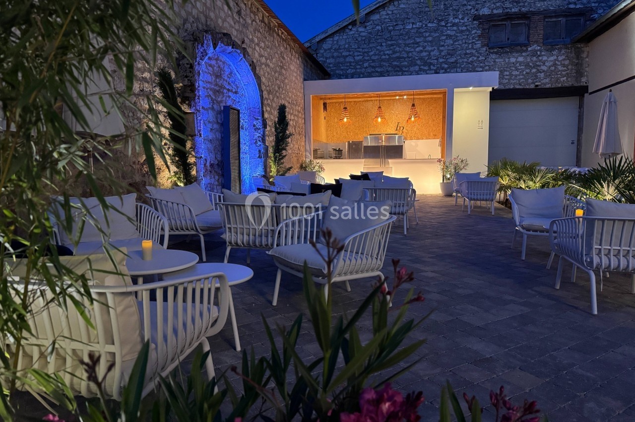 Terrasse extérieure en soirée avec mobilier moderne, éclairage chaleureux et mur en pierre en arrière-plan.