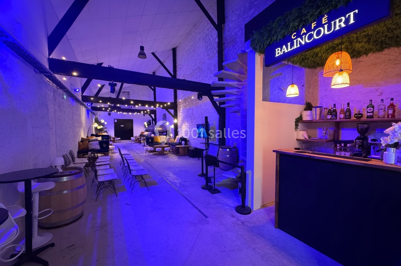 Salle lumineuse avec tables, chaises, bar éclairé et décorations suspendues dans une ambiance chaleureuse.